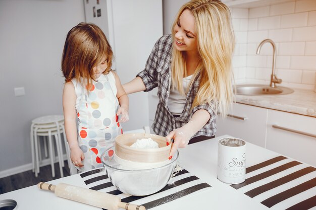 Una hermosa joven madre con su pequeña hija está cocinando en la cocina en casa