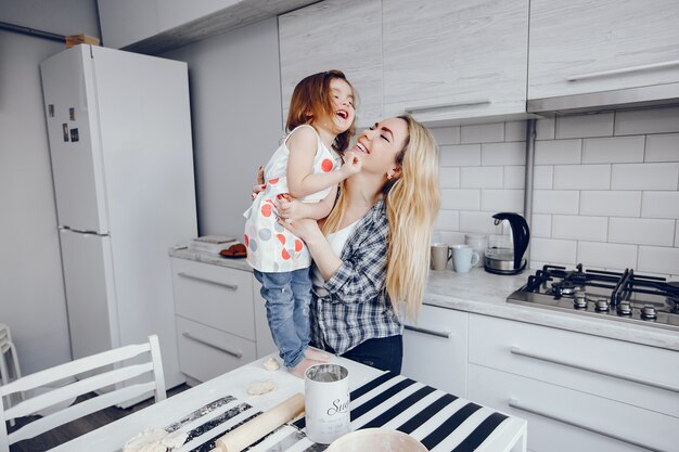 Una hermosa joven madre con su pequeña hija está cocinando en la cocina en casa