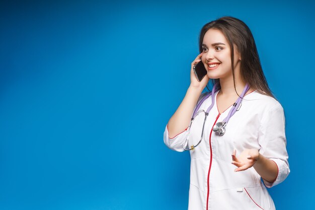 Hermosa joven médico hablando por teléfono con el paciente en azul.