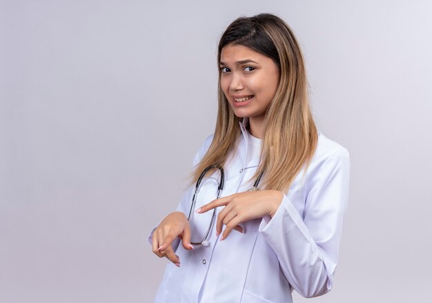 Hermosa joven médico vistiendo bata blanca con estetoscopio levantando las palmas en gesto de rechazo con expresión de disgusto