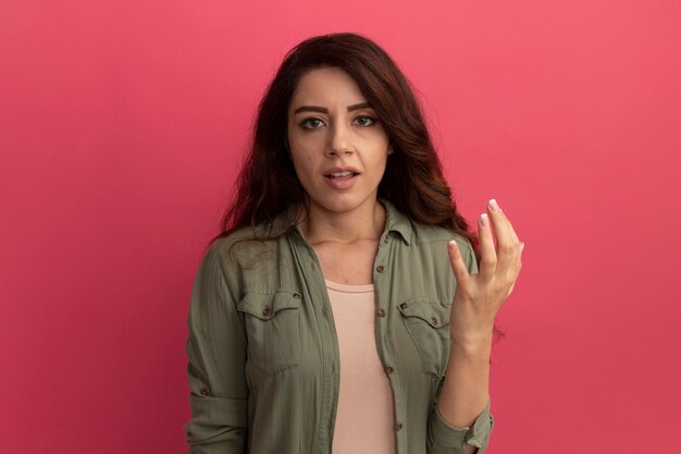 Hermosa joven mirando al frente vistiendo camiseta verde oliva aislada en la pared rosa