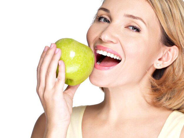 Hermosa joven mordiendo el morder una manzana madura fresca - en la pared blanca.
