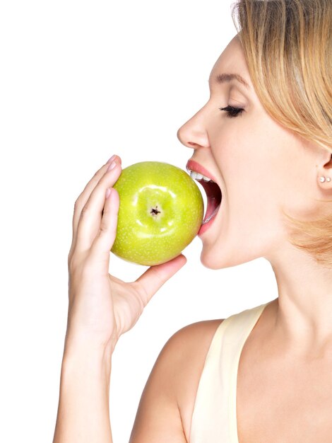 Hermosa joven mordiendo el morder una manzana madura fresca - en la pared blanca.