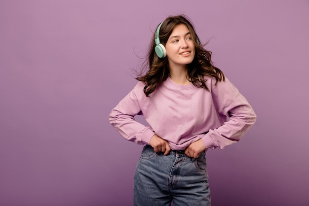 Hermosa joven morena caucásica posando con auriculares mirando hacia otro lado sobre fondo púrpura con espacio para texto Concepto de dispositivo tecnológico