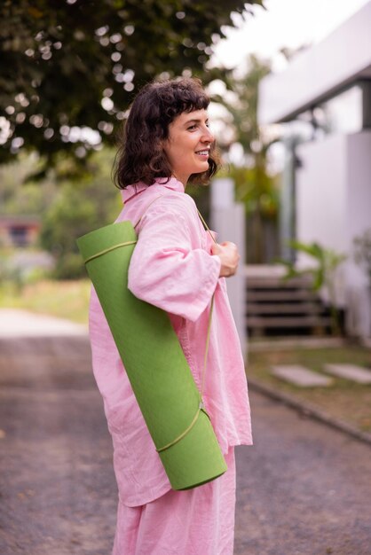 Hermosa joven morena caucásica sosteniendo esterilla de yoga preparándose para hacer ejercicio al aire libre Estilo de vida saludable mantenerse en forma concepto