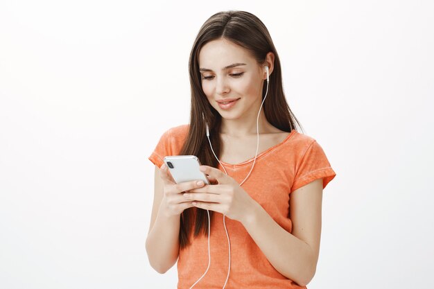 Hermosa joven morena escuchando música en auriculares y sosteniendo el teléfono móvil