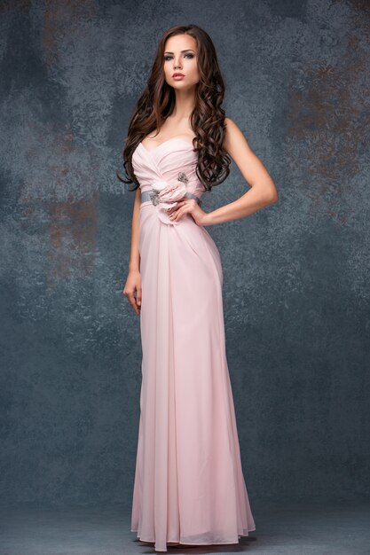 Hermosa joven morena con el pelo posando en un vestido largo rosa ai.