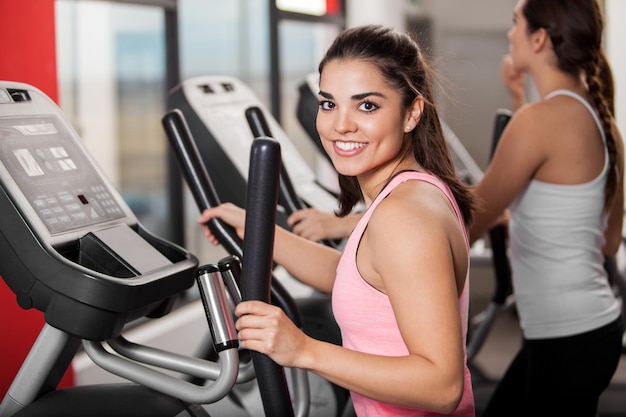 Foto gratuita hermosa joven morena trabajando en un entrenador elíptico y sonriendo