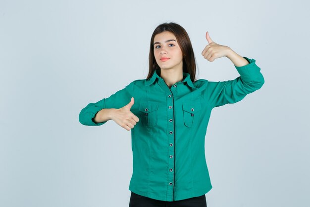 Hermosa joven mostrando doble pulgar hacia arriba en camisa verde y luciendo orgullosa, vista frontal.