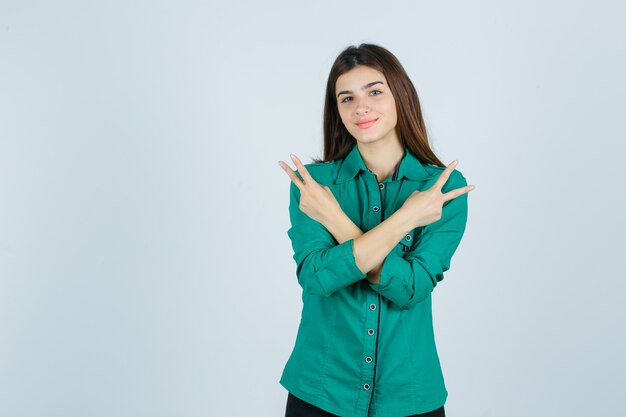 Hermosa joven mostrando gesto de paz en camisa verde y mirando alegre, vista frontal.