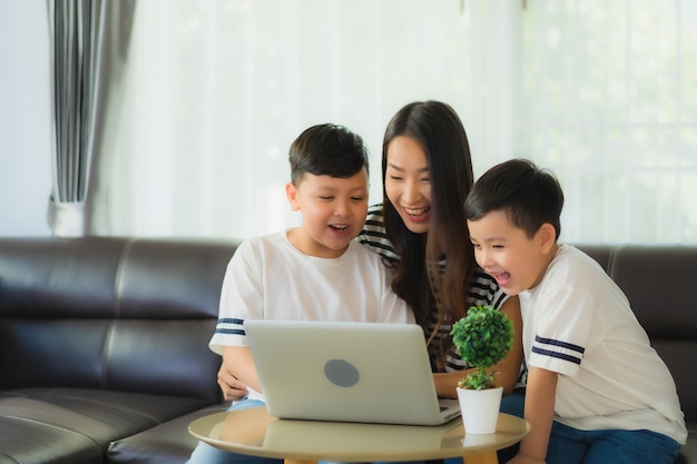 Hermosa joven mujer asiática mamá con 2 su hijo usar laptop o computadora portátil en el sofá