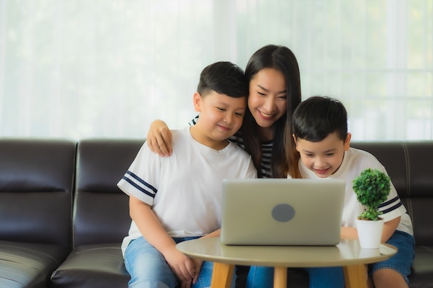 Hermosa joven mujer asiática mamá con sus dos hijos usando la computadora portátil en el sofá