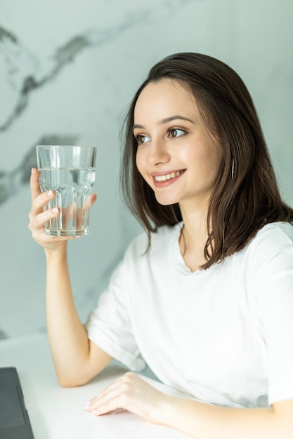 Hermosa joven mujer bonita sostiene un vaso con agua en la cocina