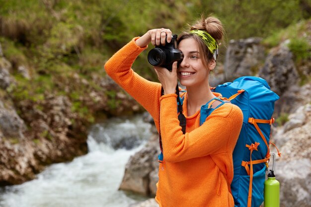 Hermosa joven mujer caucásica hace fotos en la cámara moderna, lleva diadema, puente naranja