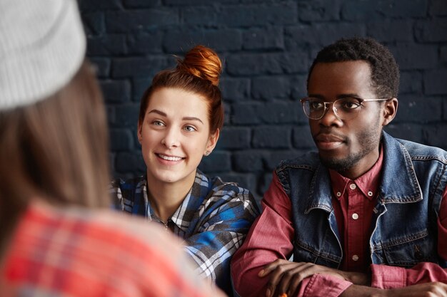 Hermosa joven mujer caucásica con sonrisa alegre y hipster masculino africano con gafas