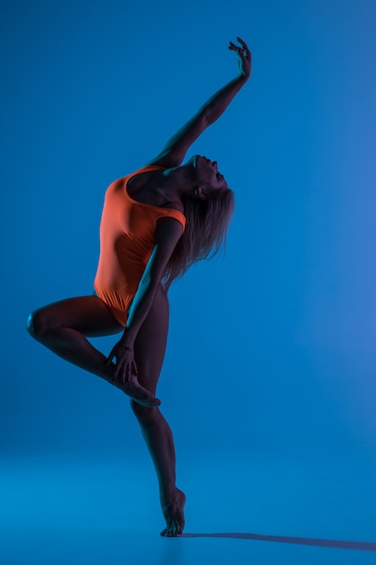 Hermosa y joven mujer gimnasta en forma con vestido azul de ropa deportiva trabajando, realizando un elemento de gimnasia artística, saltando, haciendo un salto dividido en el aire, bailando