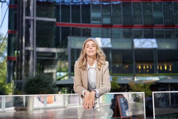 Foto gratuita hermosa joven mujer de negocios de pie en traje beige en la calle soleada cerca de edificios de oficinas