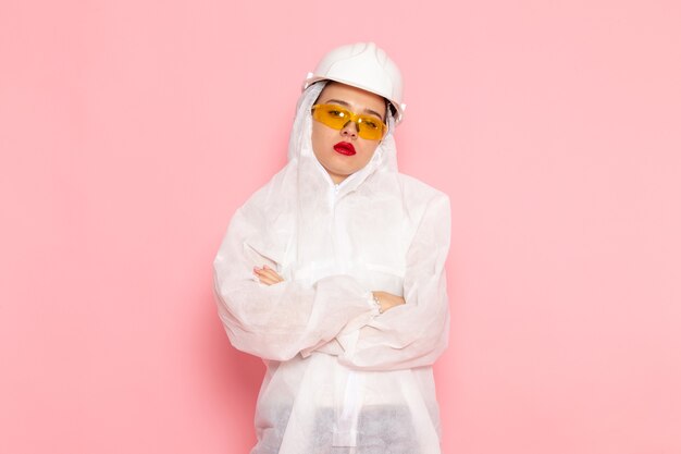 Hermosa joven mujer en traje blanco especial con casco protector aburrido posando en rosa