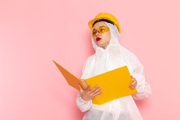 Hermosa joven mujer en traje blanco especial con casco protector sosteniendo archivo en rosa