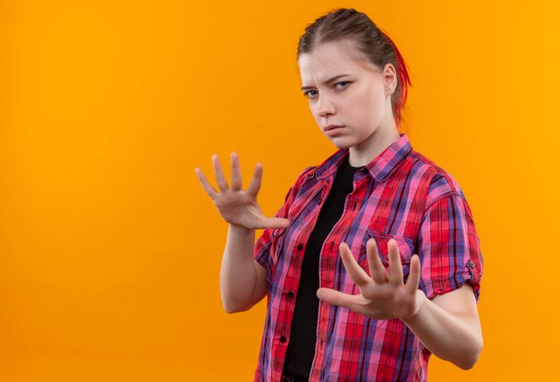 Hermosa joven mujer vistiendo camisa roja mostrando gesto de parada en pared amarilla aislada con espacio de copia