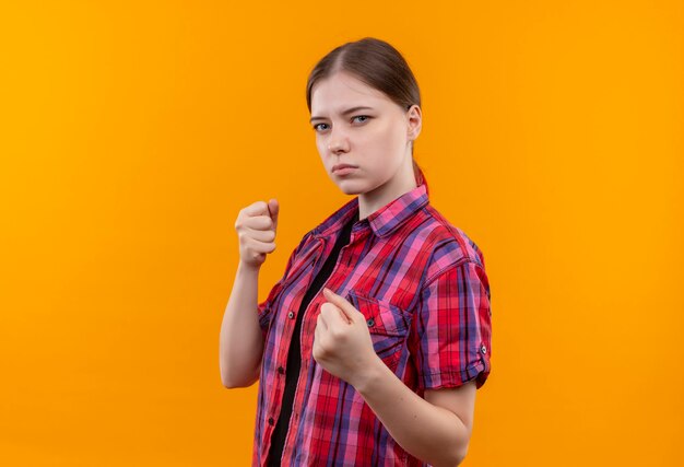 Hermosa joven mujer vistiendo camisa roja de pie en pose de lucha en la pared amarilla aislada con espacio de copia