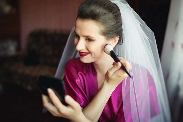 Hermosa joven novia con maquillaje de boda y peinado en el dormitorio