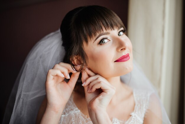 Hermosa joven novia con maquillaje de boda y peinado en el dormitorio