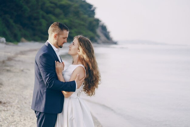 hermosa joven novia de pelo largo en vestido blanco con su joven esposo en la playa