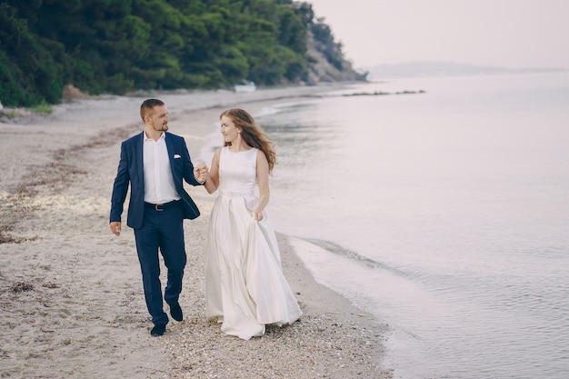 hermosa joven novia de pelo largo en vestido blanco con su joven esposo en la playa