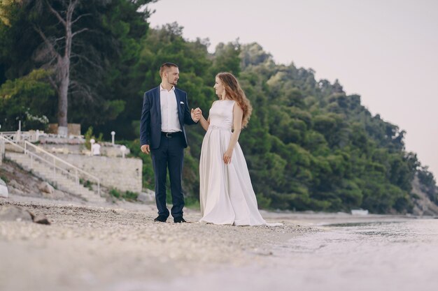 hermosa joven novia de pelo largo en vestido blanco con su joven esposo en la playa