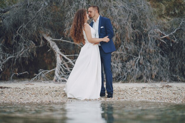 hermosa joven novia de pelo largo en vestido blanco con su joven esposo en la playa