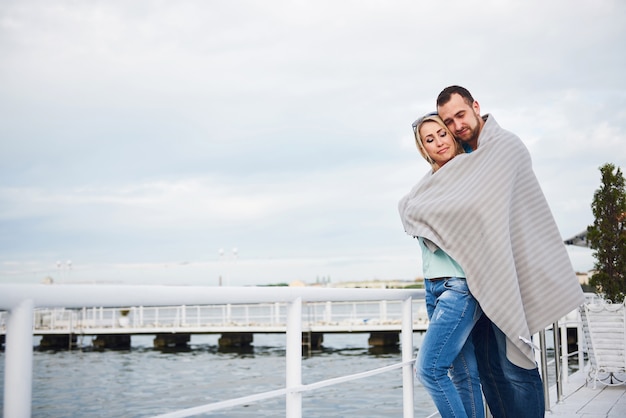 Hermosa joven pareja abrazándose, de pie en un muelle cerca del agua.