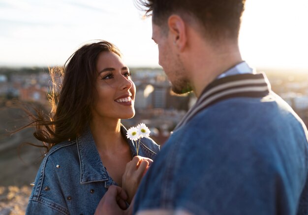 Hermosa joven pareja en el amor de pie en la azotea de un edificio en la puesta del sol.