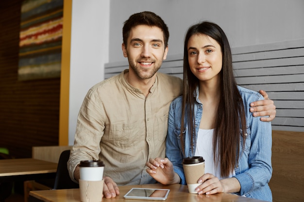 Foto gratuita hermosa joven pareja con cabello oscuro en ropa casual sonríe, bebe café y posa para una foto en un artículo de la universidad sobre el proyecto de inicio en perspectiva.