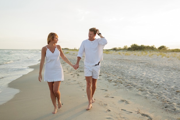 Hermosa joven pareja camina por la orilla del mar al atardecer.