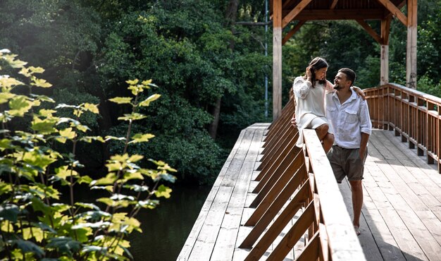 Una hermosa joven pareja se comunica en un puente en el bosque, una cita en la naturaleza, una historia de amor.
