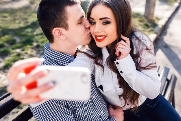 Hermosa joven pareja divirtiéndose en un banco en el parque