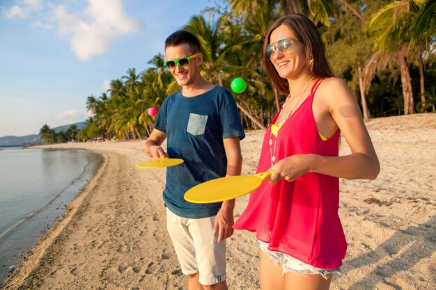 Hermosa joven pareja de enamorados jugando al ping pong en la playa tropical, divirtiéndose, vacaciones de verano, activo, sonriente, divertido, positivo