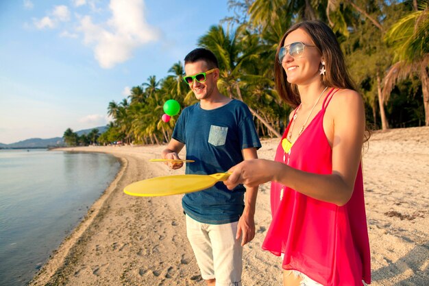 Hermosa joven pareja de enamorados jugando al ping pong en la playa tropical, divirtiéndose, vacaciones de verano, activo, sonriente, divertido, positivo