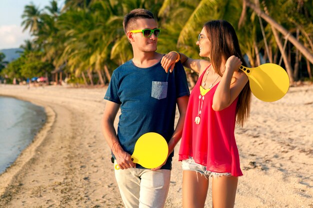 Hermosa joven pareja de enamorados jugando al ping pong en la playa tropical, divirtiéndose, vacaciones de verano, activo, sonriente, divertido, positivo