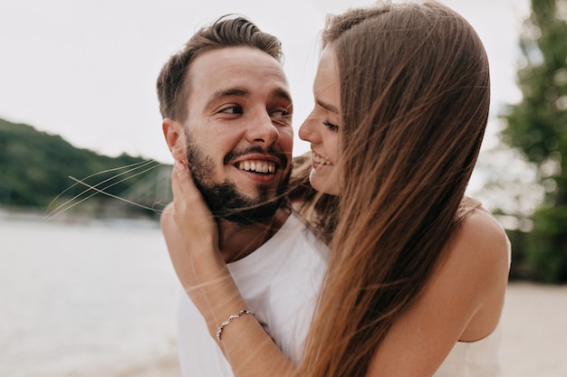 Hermosa joven pareja está hablando y sonriendo mientras camina por la playa en un día soleado