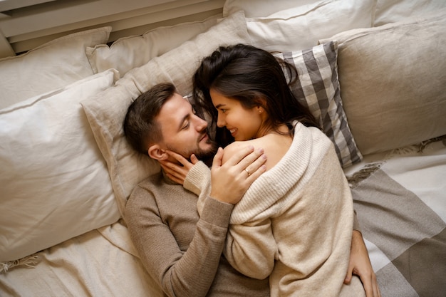 Hermosa joven pareja feliz descansando en la cama y sonriendo, abrazando