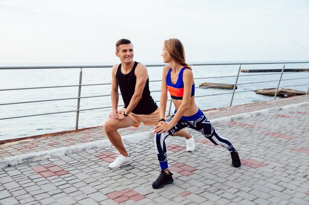 Hermosa joven pareja haciendo ejercicios de deportes, mirando el uno al otro, estirando el cuerpo