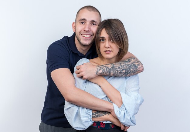 Hermosa joven pareja hombre y mujer abrazando feliz y positivo sonriendo de pie sobre la pared blanca