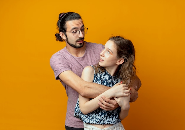 Hermosa joven pareja hombre y mujer felices enamorados abrazándose juntos de pie sobre la pared naranja