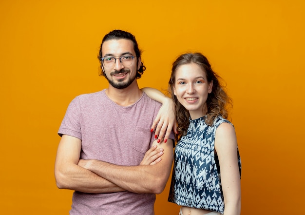 Hermosa joven pareja hombre y mujer felices enamorados de pie sobre la pared naranja