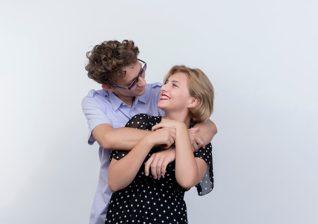 Hermosa joven pareja hombre y mujer feliz enamorado abrazándose de pie sobre la pared blanca