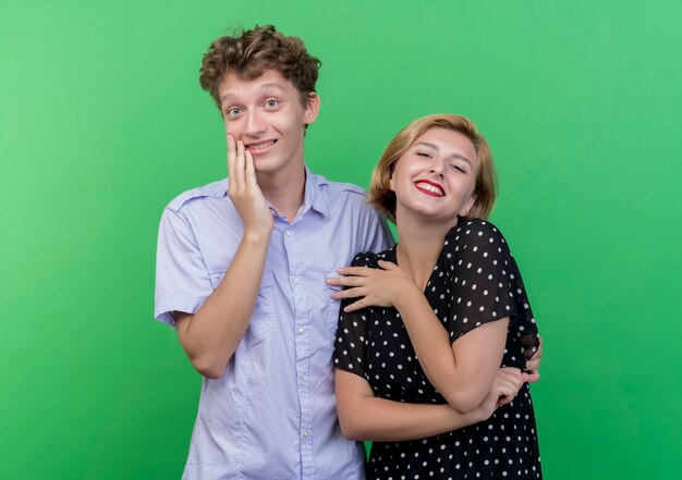 Hermosa joven pareja hombre y mujer feliz y positivo sonriendo alegremente de pie sobre la pared verde