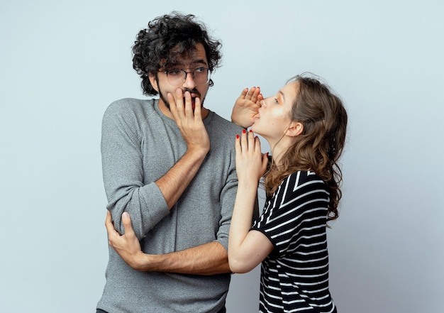 Foto gratuita hermosa joven pareja hombre y mujer, mujer susurrando secretos o chismes interesantes a su novio sobre la pared blanca