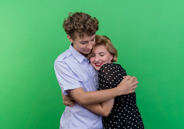 Hermosa joven pareja hombre y mujer de pie juntos hapy enamorado abrazándose de pie sobre la pared verde